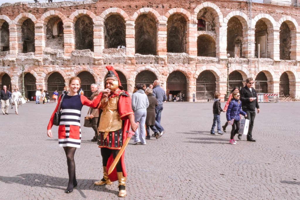 A girl with a Roman kissing her hand in front of Verona Arena