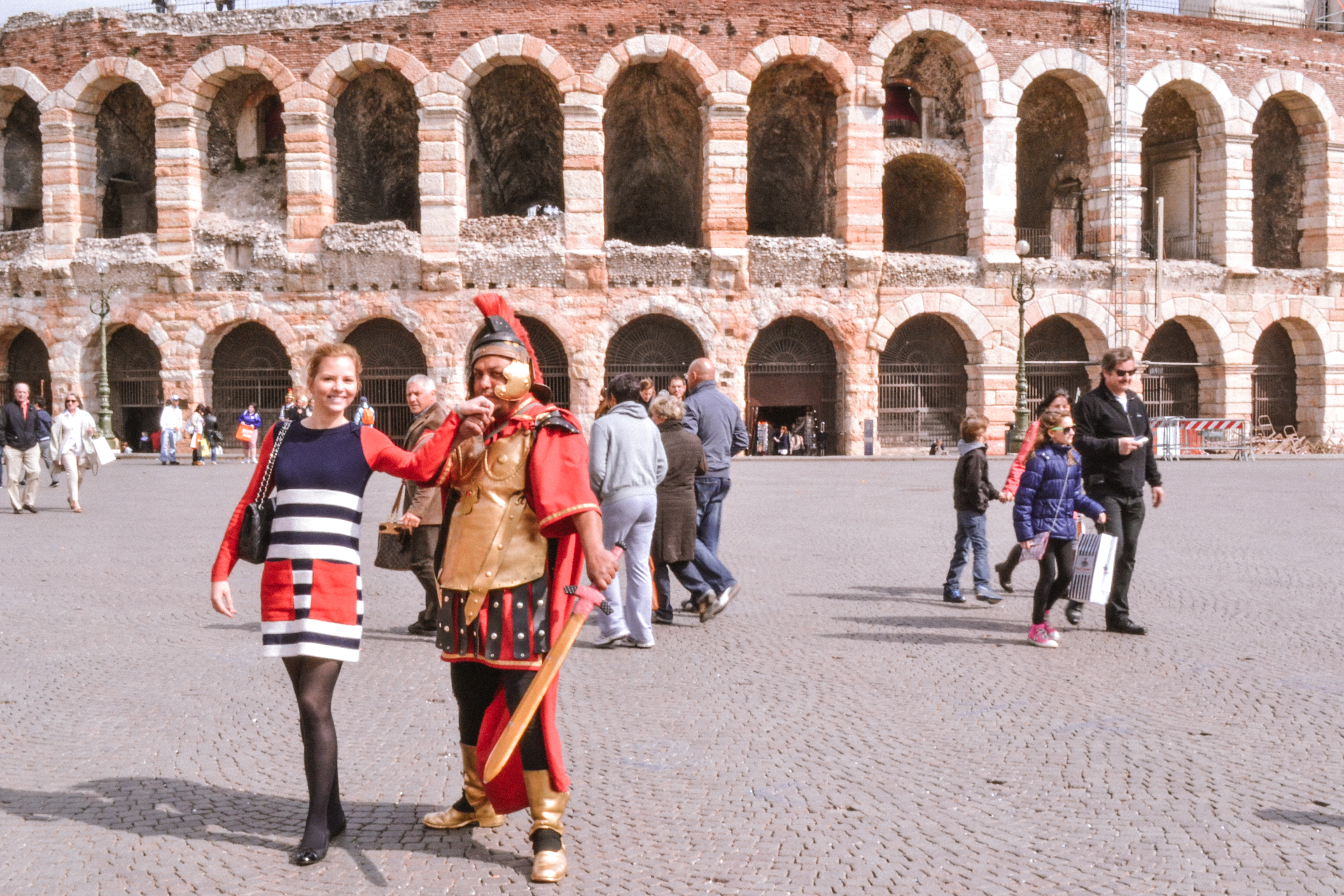 A girl with a Roman kissing her hand in front of Verona Arena