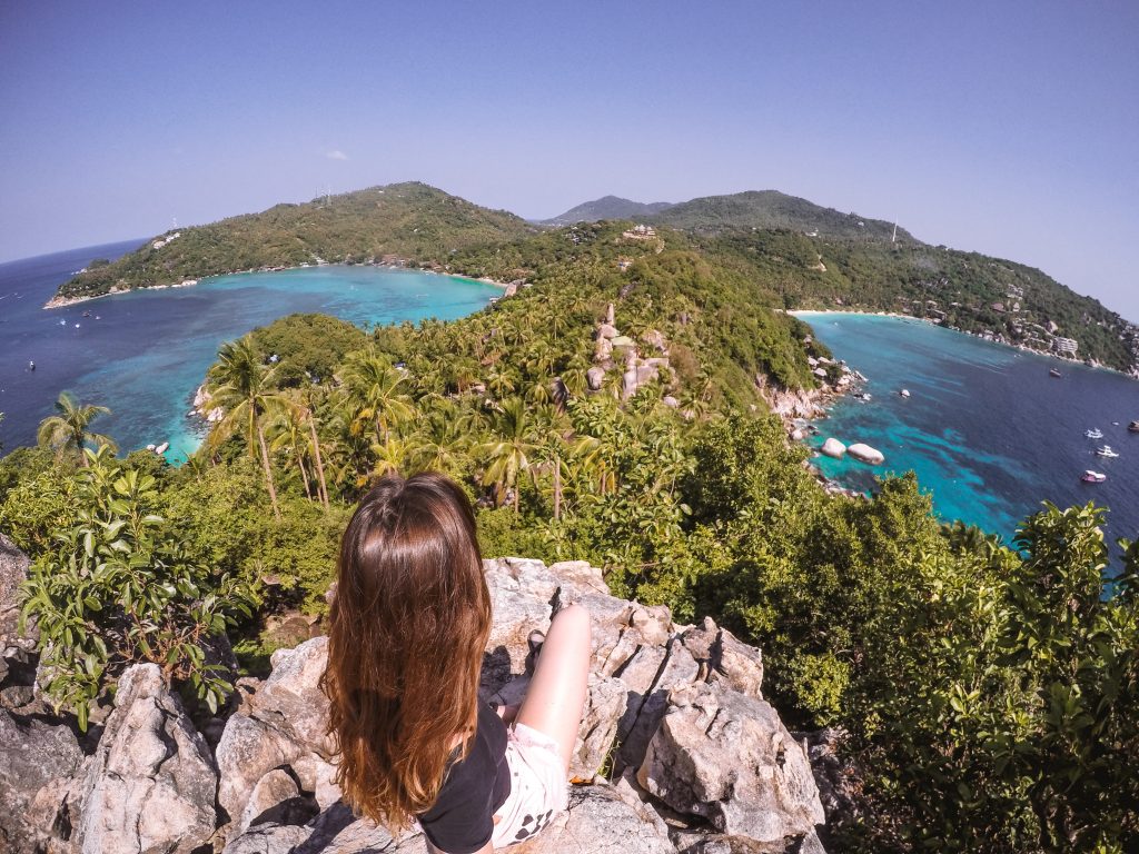 A girl sitting on a cliff overlooking the palm tree forest and the sea in Thailand