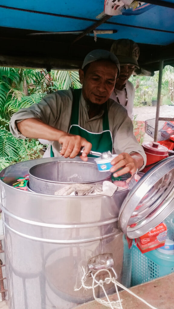 A man serving coconut ice-cream from a metal canister in Thailand